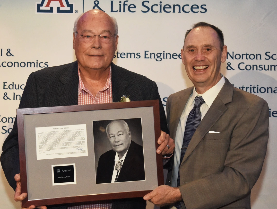 Picture of alumni and dean holding up award